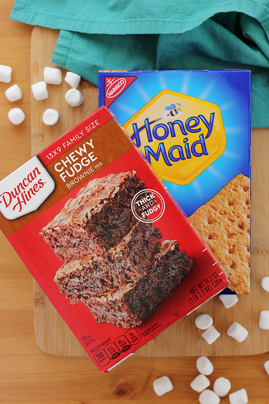 boxed brownie mix, box of graham crackers, and mini marshmallows on a wooden cutting board. 