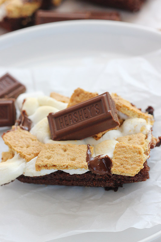 closeup image of a brownie sitting on a white plate topped with marshmallow, melted chocolate and graham crackers