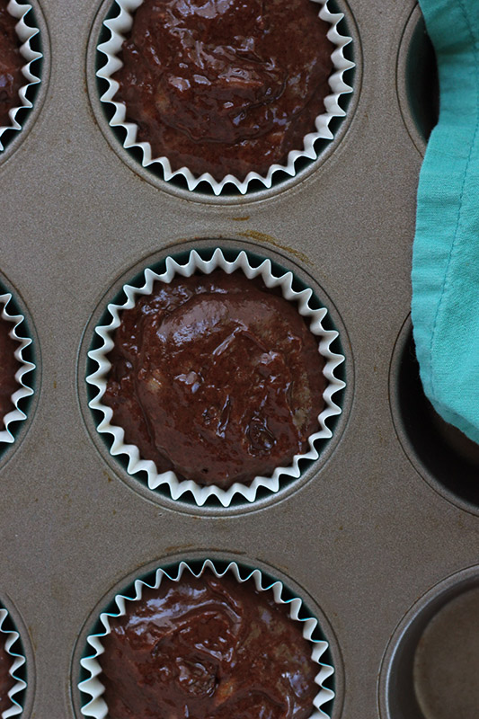 chocolate muffin batter spooned into paper liners inside of a baking tray