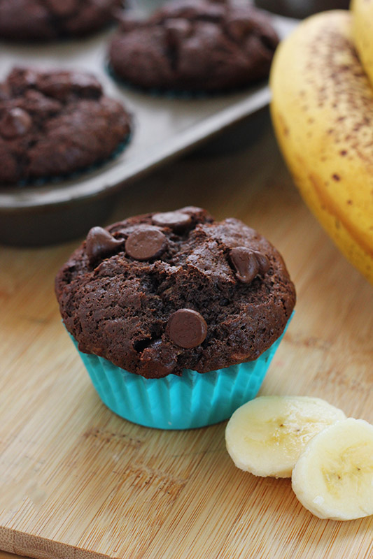single chocolate muffin with banana slices on the side sitting on a wooden cutting board