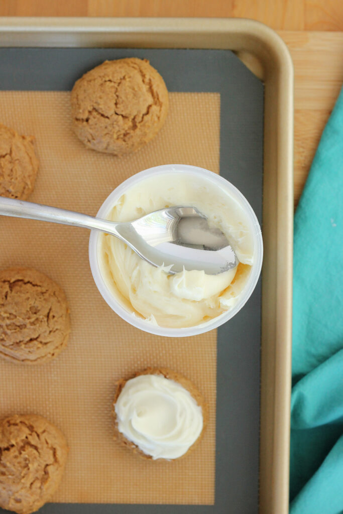cookies on a baking tray with a can of frosting and a spoon