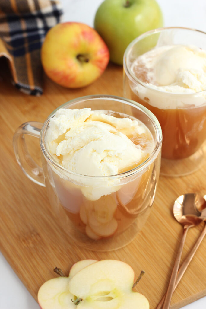 glass mugs filled with apple cider and scoops of vanilla ice cream on top of a wooden cutting board