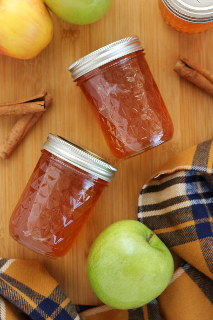 two jars of jelly on a wooden cutting board with cinnamon sticks and apples
