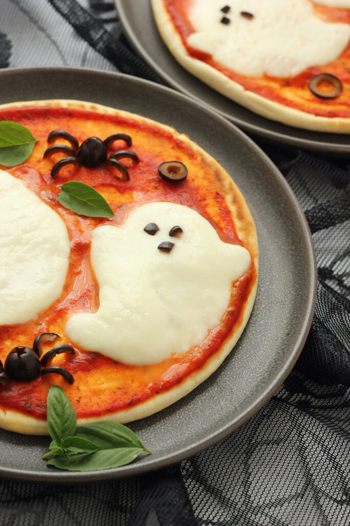 side image of a pizza topped with a cheese ghost shape and a spider olive