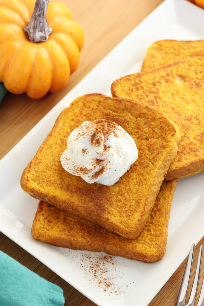 slices of french toast on a white plate with one topped with whipped cream and cinnamon