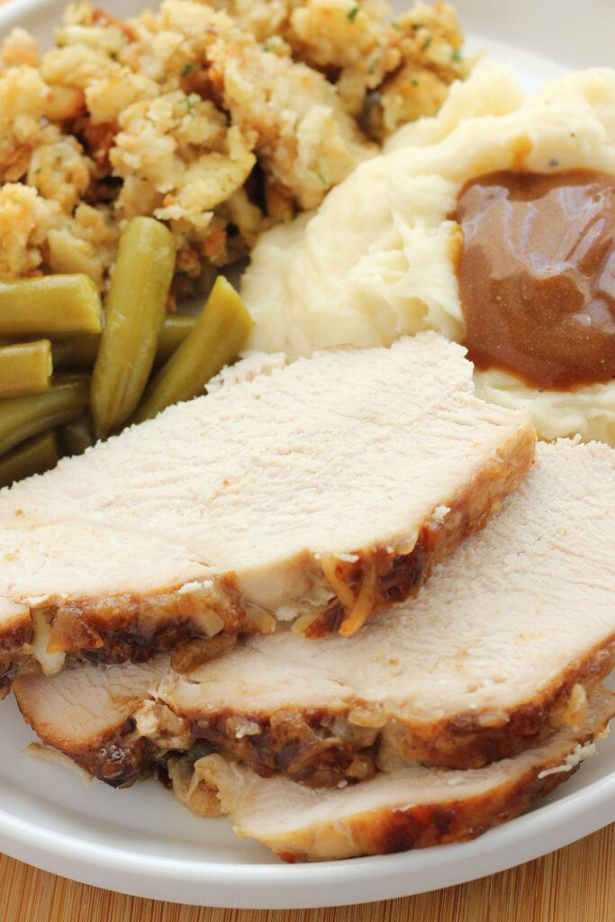 close up image of a stack of turkey slices on a white plate with stuffing and other sides
