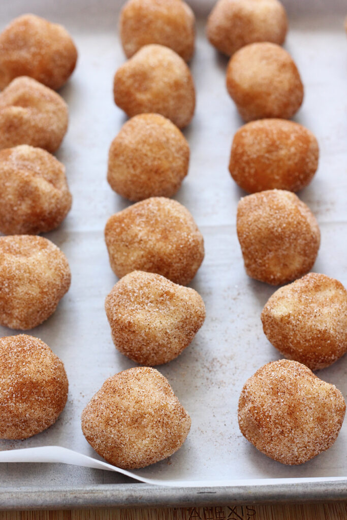 cookie dough balls rolled in cinnamon and sugar on a baking tray