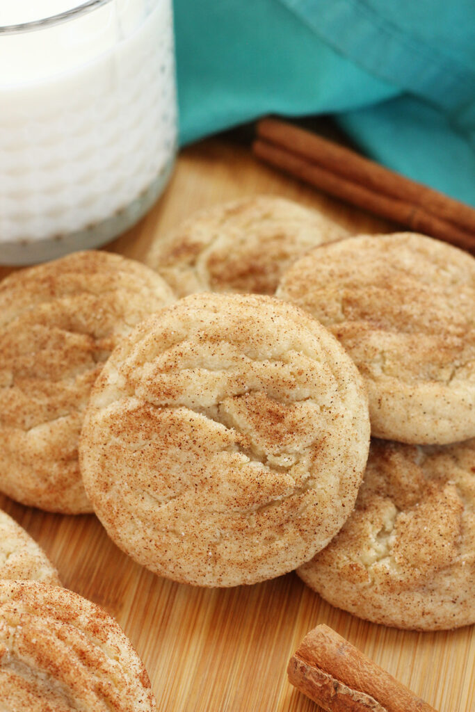 stack of cinnamon sugar cookies on a wooden cutting board with cinnamon sticks and glass of milk
