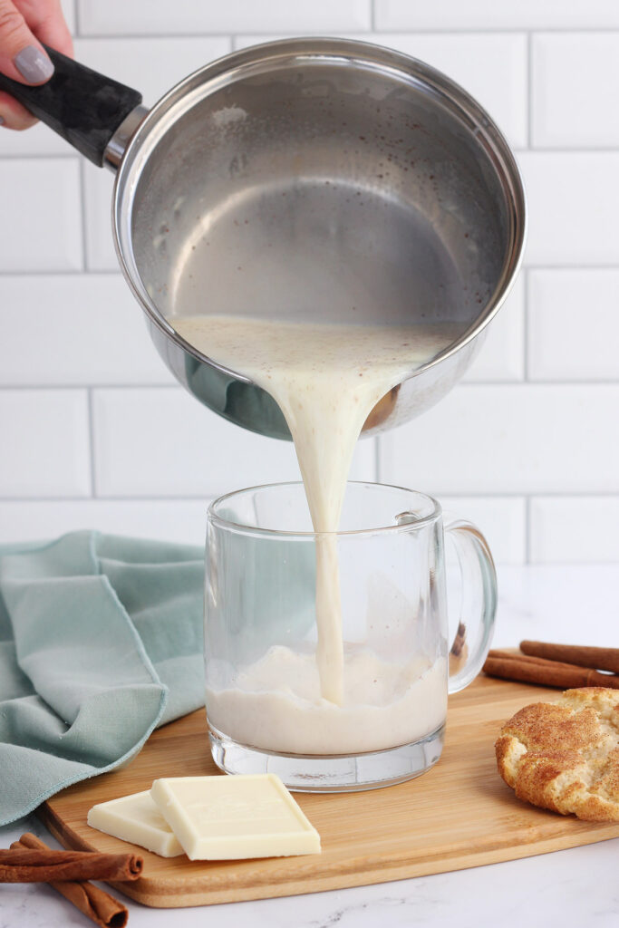 white hot chocolate being poured from a pan to a glass mug