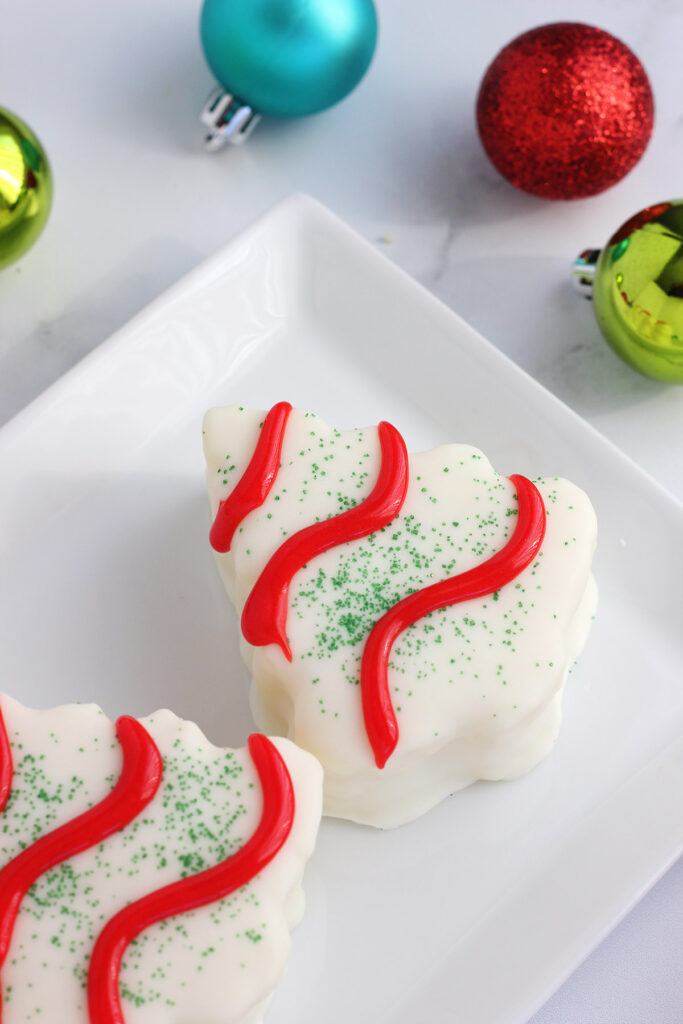 close up image of a christmas tree cake on a white plate with holiday decorations surrounding