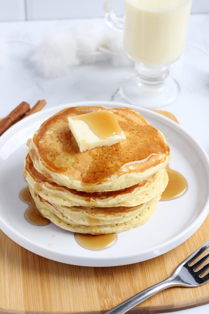 stack of pancakes on a white plate with syrup and butter