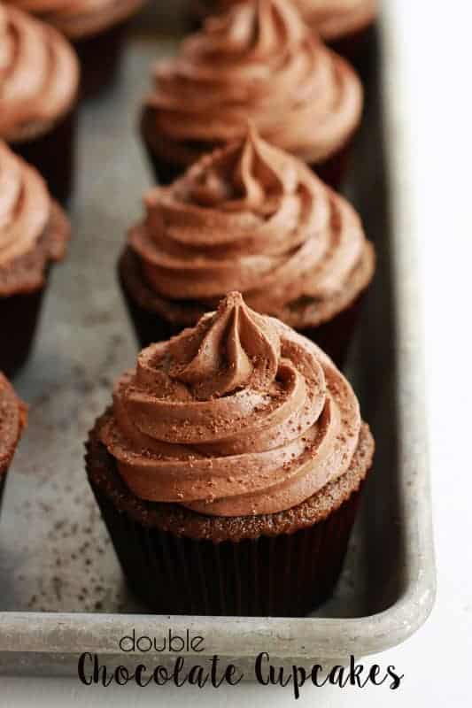 Baking tray filled with baked cupcakes that have frosting piped onto the top