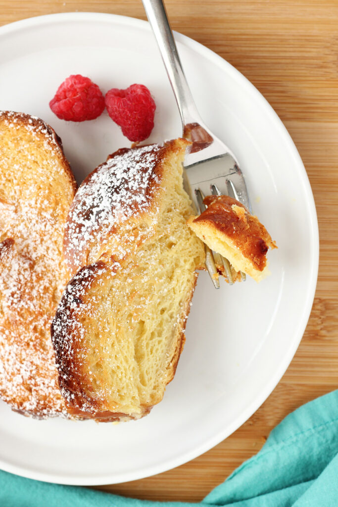 two slices of french toast on a white plate dusted in powdered sugar with a bite on a fork