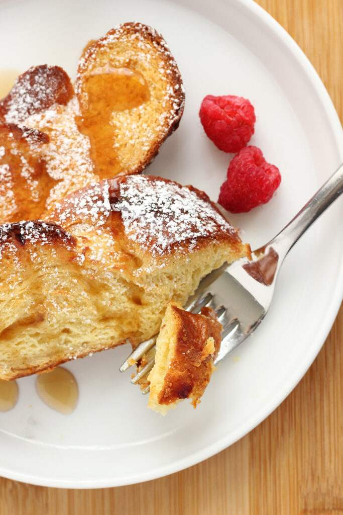 french toast on a white plate with berries and a bite on top of a fork