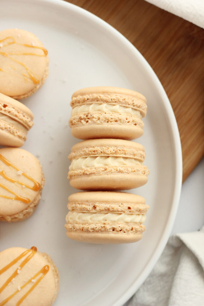 stack of caramel macarons on a white plate with salt sprinkled around