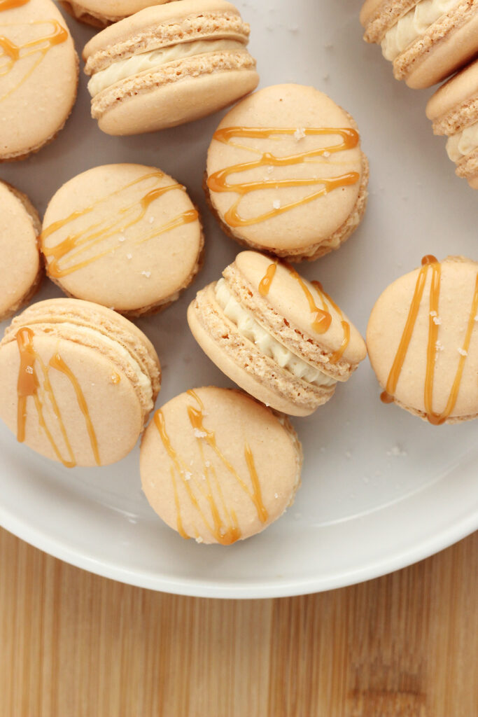 white plate stacked with French macarons that have been drizzled in caramel and sprinkled with salt