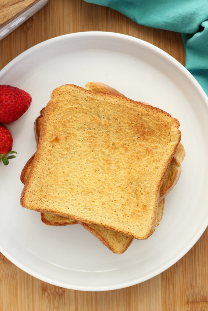 stack of cooked french toast on a white plate with fresh strawberries