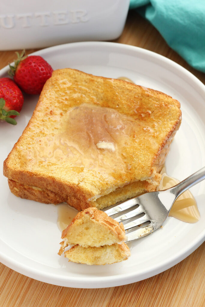 two slices of French toast with syrup on a white plate with a bite sitting on a fork
