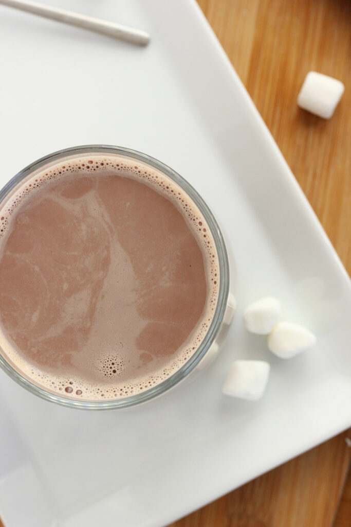 top down image of a mug filled with hot chocolate sitting on a white plate with marshmallows on the side