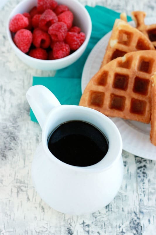 syrup dispenser sitting on a wooden table with a side of waffles