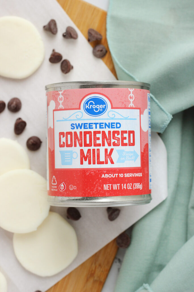 can of sweetened condensed milk on a wooden cutting board with chocolate chips and a blue napkin