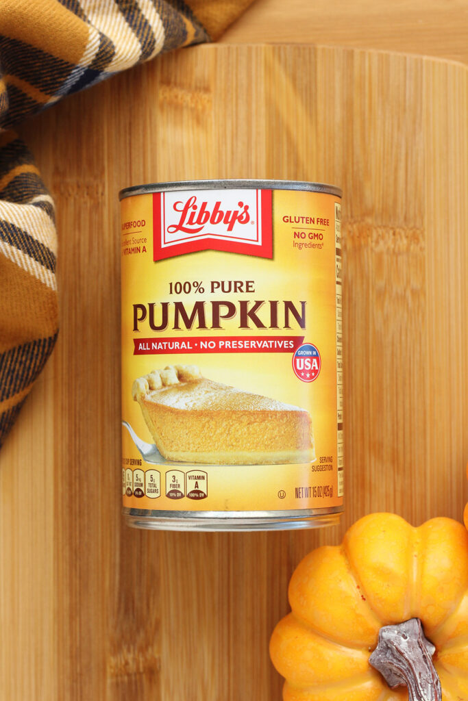 can of pumpkin puree on a wooden cutting board with a fall colored stripe towel