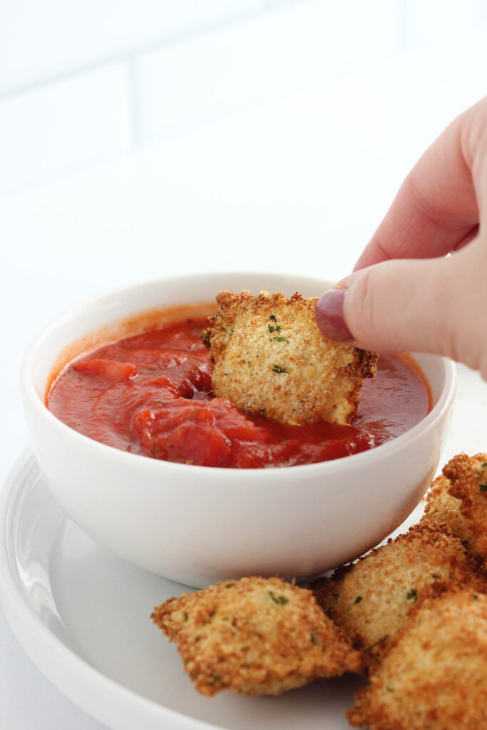 single ravioli being dipped into marinara