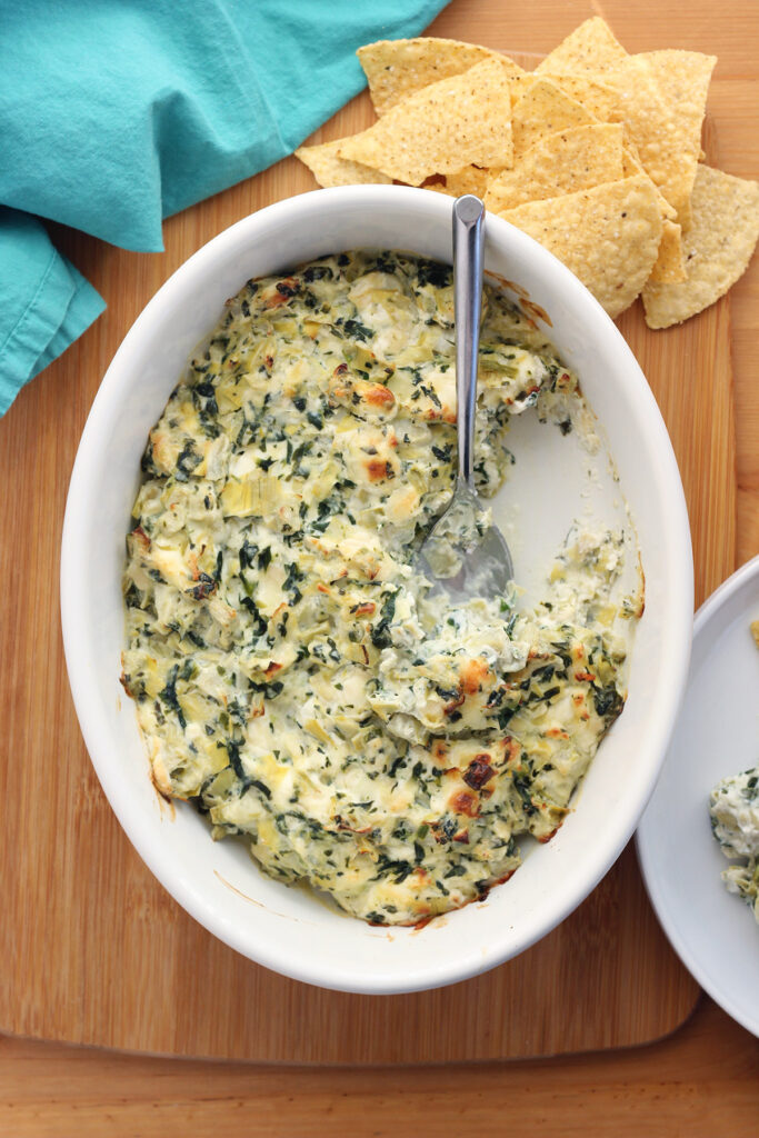 glass dish filled with warm cheese dip with a spoon and chips