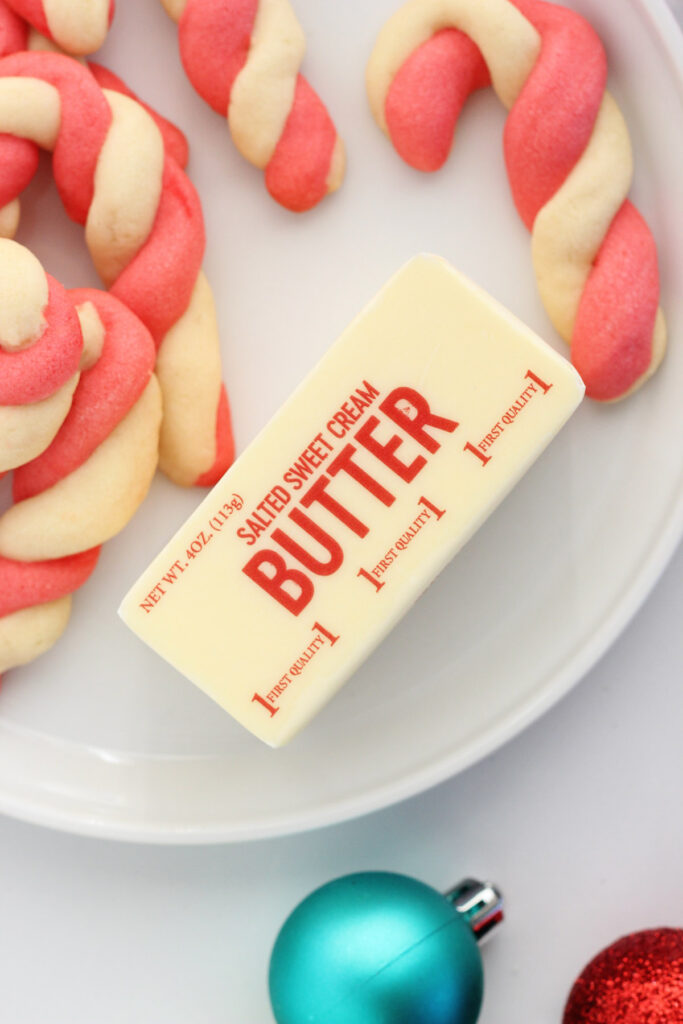 salted butter on a white plate with red and white cookies shaped like candy canes