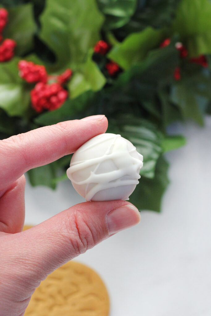 fingers holding a truffle covered in white chocolate