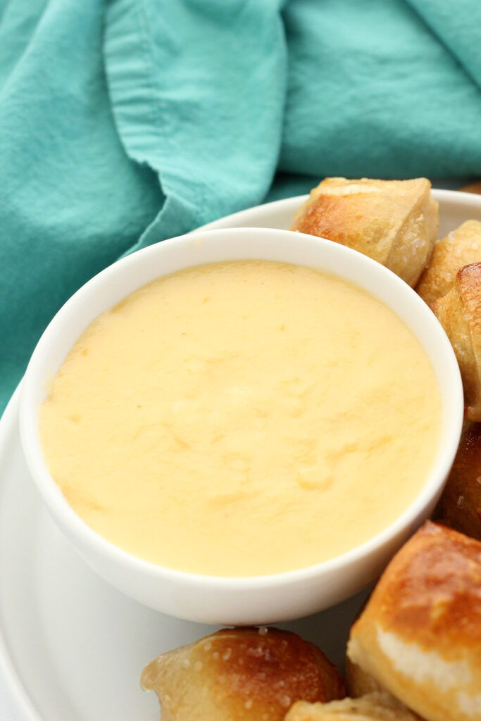 beer cheese dip recipe in a white bowl on a plate that is filled with pretzel bites