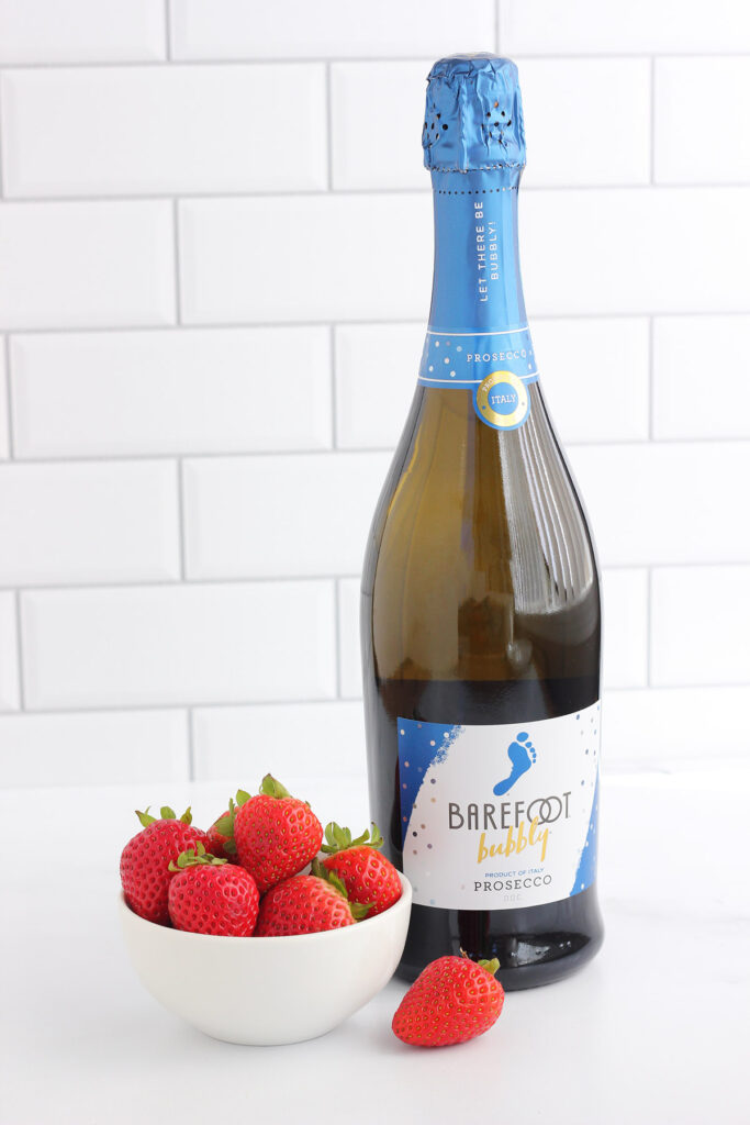 bottle of barefoot prosecco and a  bowl of strawberries on a white table
