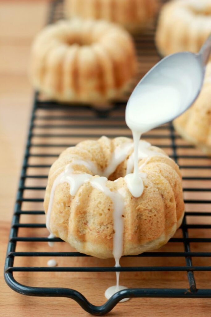 spoon drizzling icing over a warm mini banana bread loaf shaped in a circle