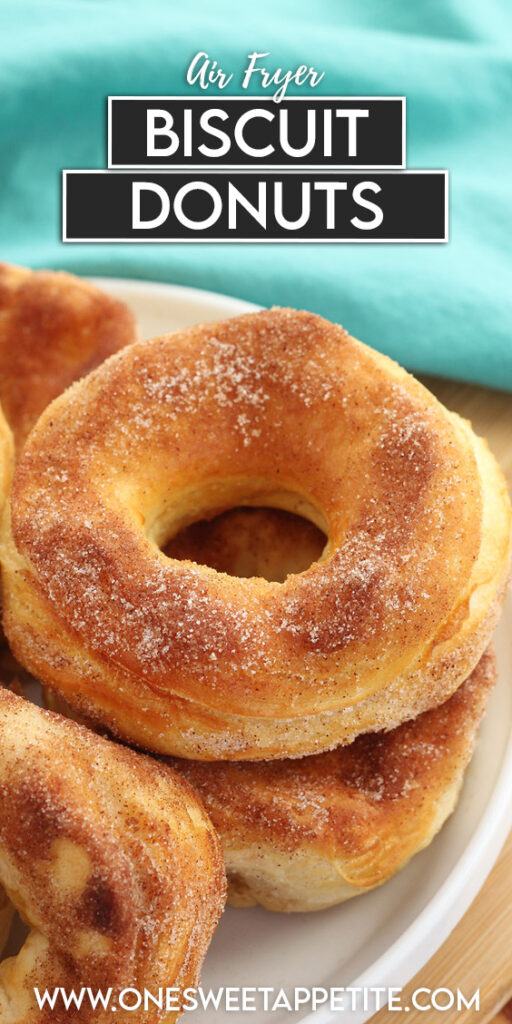 pinterest graphic image. Closeup of a donut that is sitting on a white plate with cinnamon and sugar sprinkled on top. A teal napkin is in the background sitting on a wooden cutting board. Text overlay reading "air fryer biscuit donuts. 