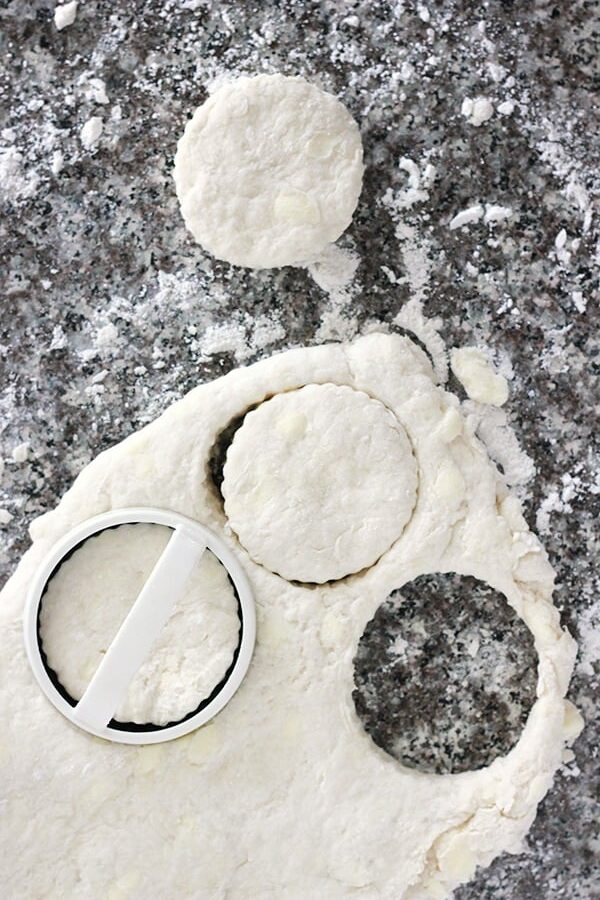 biscuit dough on a black quarts countertop  rolled out with a round cutter pressed into a portion of the dough. 