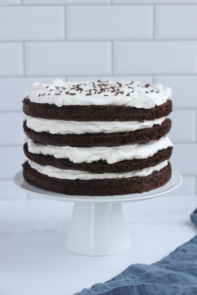 chocolate cake layered on a white cake stand with whipped cream 