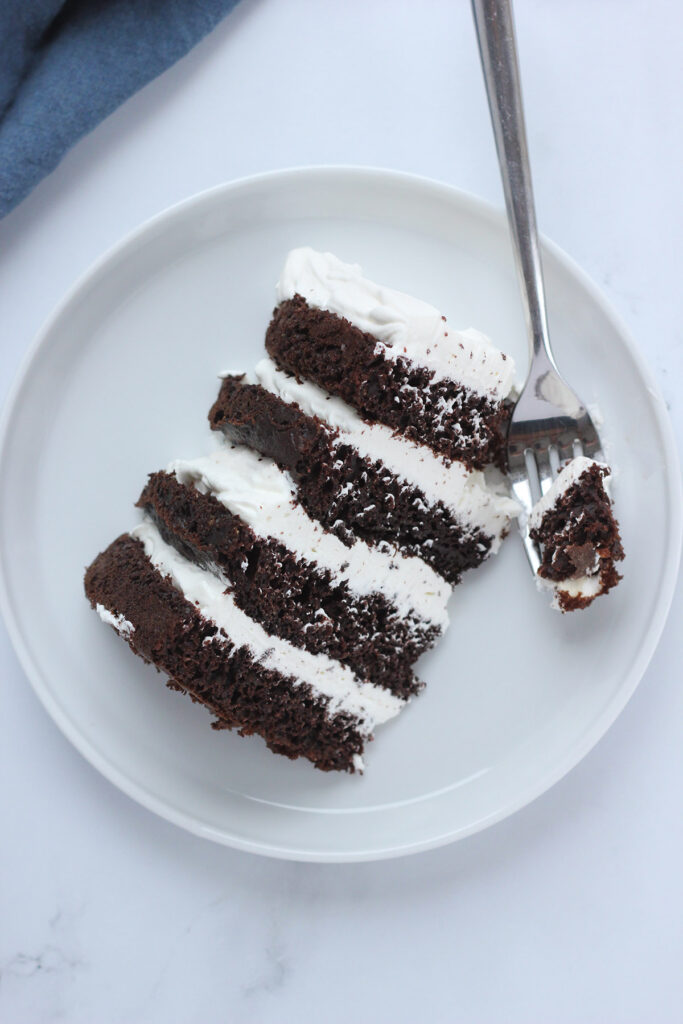 top down image of a chocolate cake layered with whipped cream one bite sitting on a fork on a white table