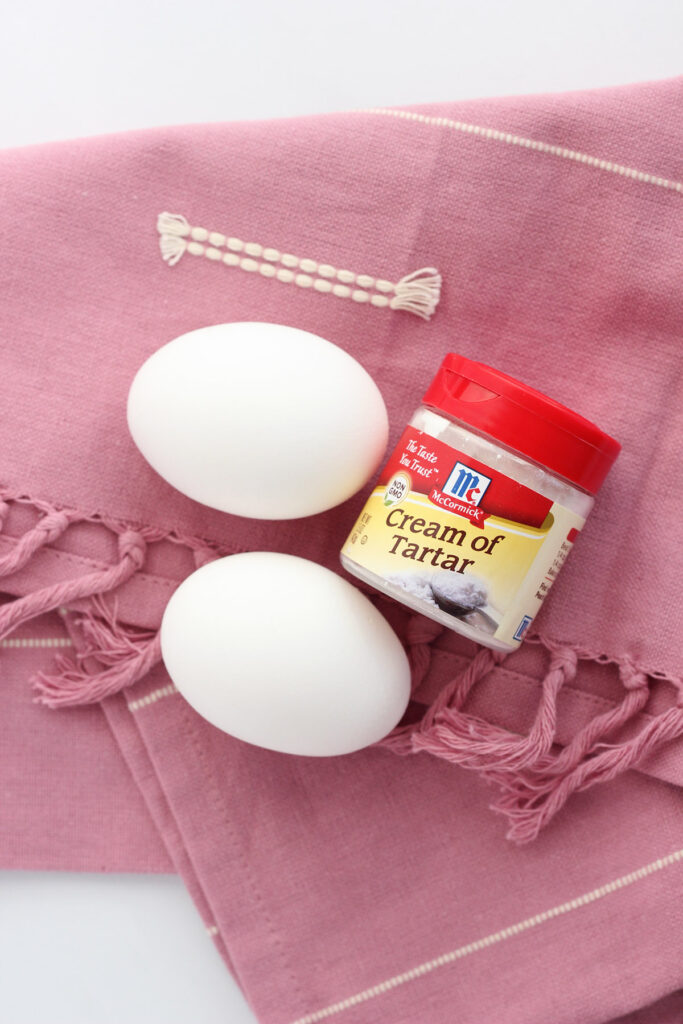 two eggs and a small container of cream of tartar sitting on a pink napkin