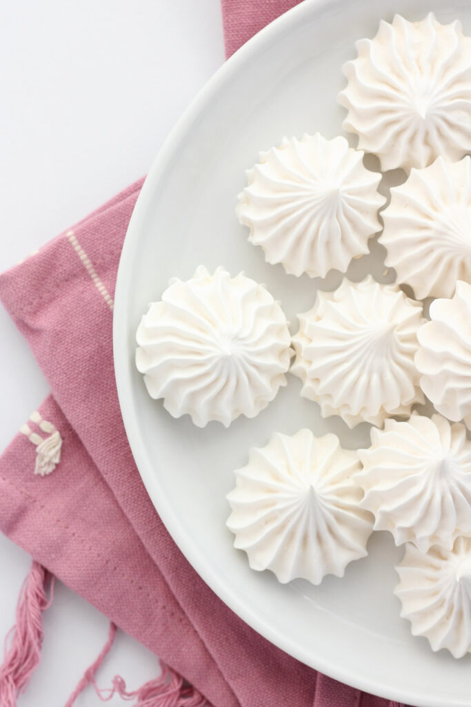 round white plate with a small lip around the edge topped with a pile of white cookies shaped like star rounds.