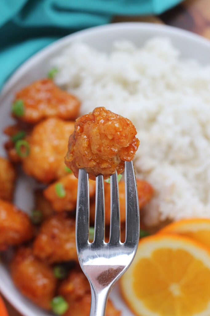 crispy chicken piece on a fork hovering over a plate of rice and chicken 