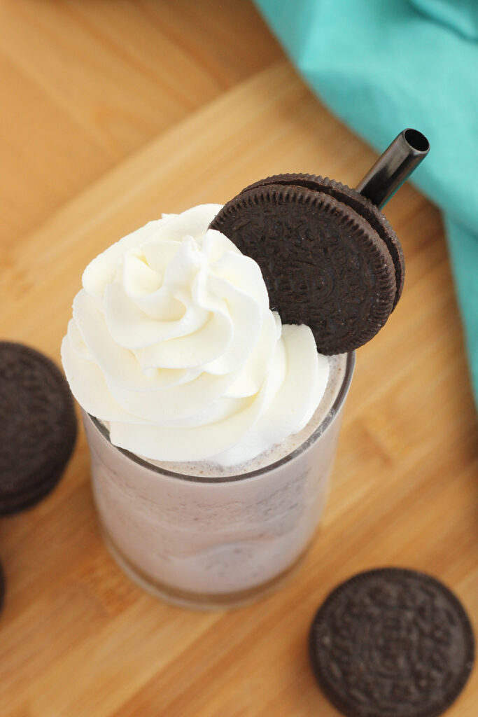top down image of a skinny glass filled with chocolate frappuccino that is topped with whipped cream and a signle cookie. 