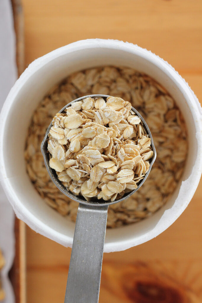 a metal measuring cup filled with oats resting on top of an open container of rolled oats