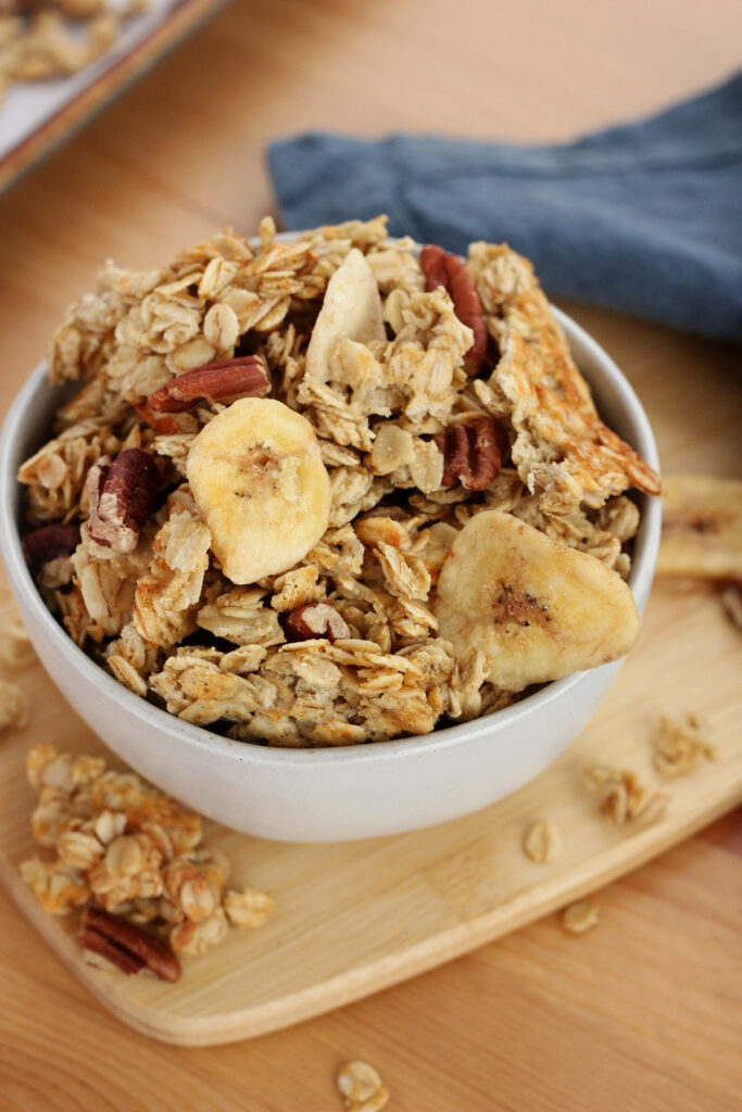 off white bowl sitting on a wooden cutting board overflowing with granola 