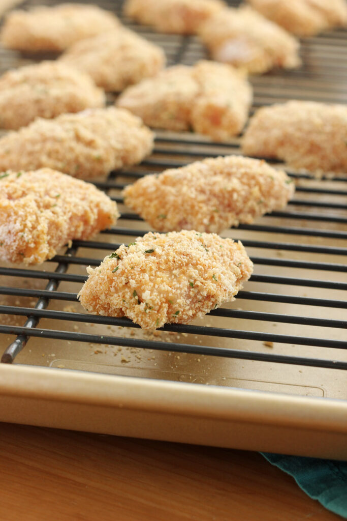 unbaked chicken nuggets covered in breadcrumbs sitting on a baking tray