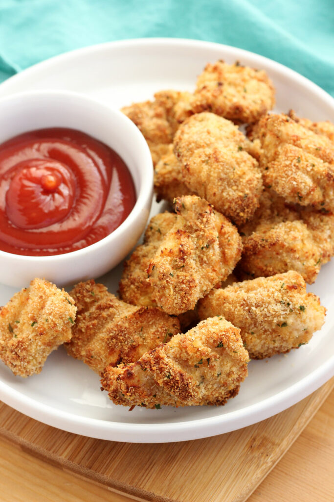 white plate topped with golden brown chicken nuggets and a small white bowl filled with ketchup