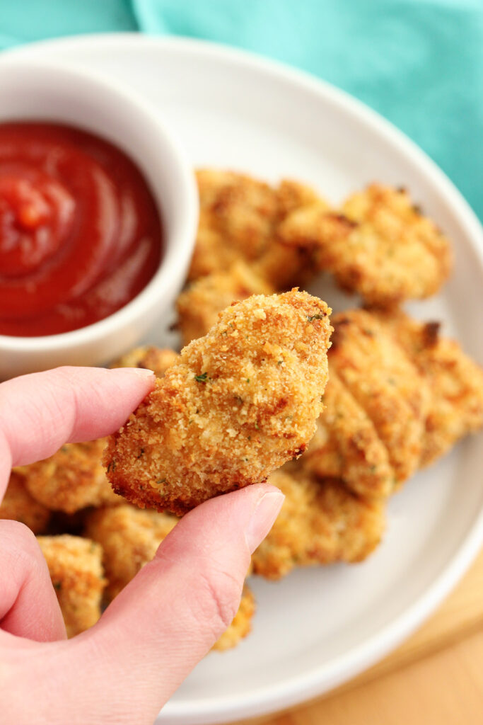 single chicken nugget being held above a plate of nuggets