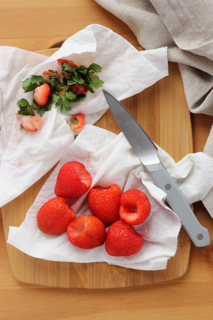 washed strawberries sitting on a white napkin with a pairing knife. The berries have been hulled and have a hole ready to be filled