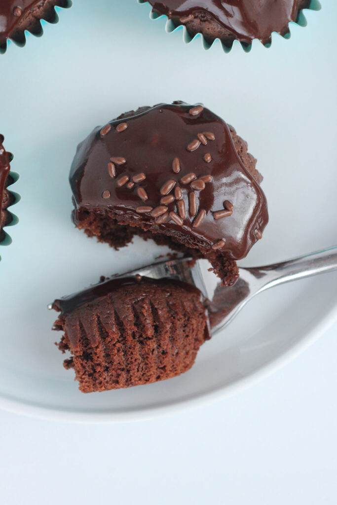 chocolate cupcake with a bite sitting on a fork on top of a white round plate