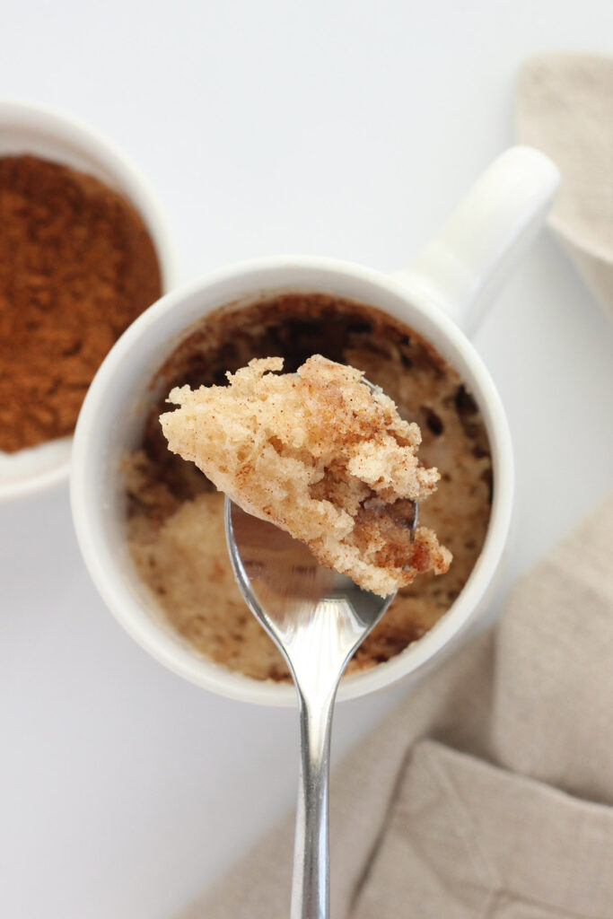 white mug filled with cinnamon cake with a single bite sitting on a spoon. 