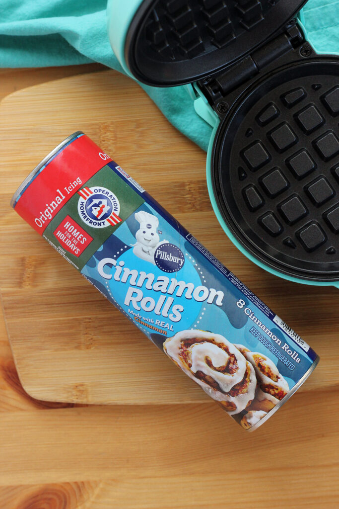 can of  pilsbury cinnamon rolls sitting on a wooden tabletop with an open waffle iron sitting off to the side.